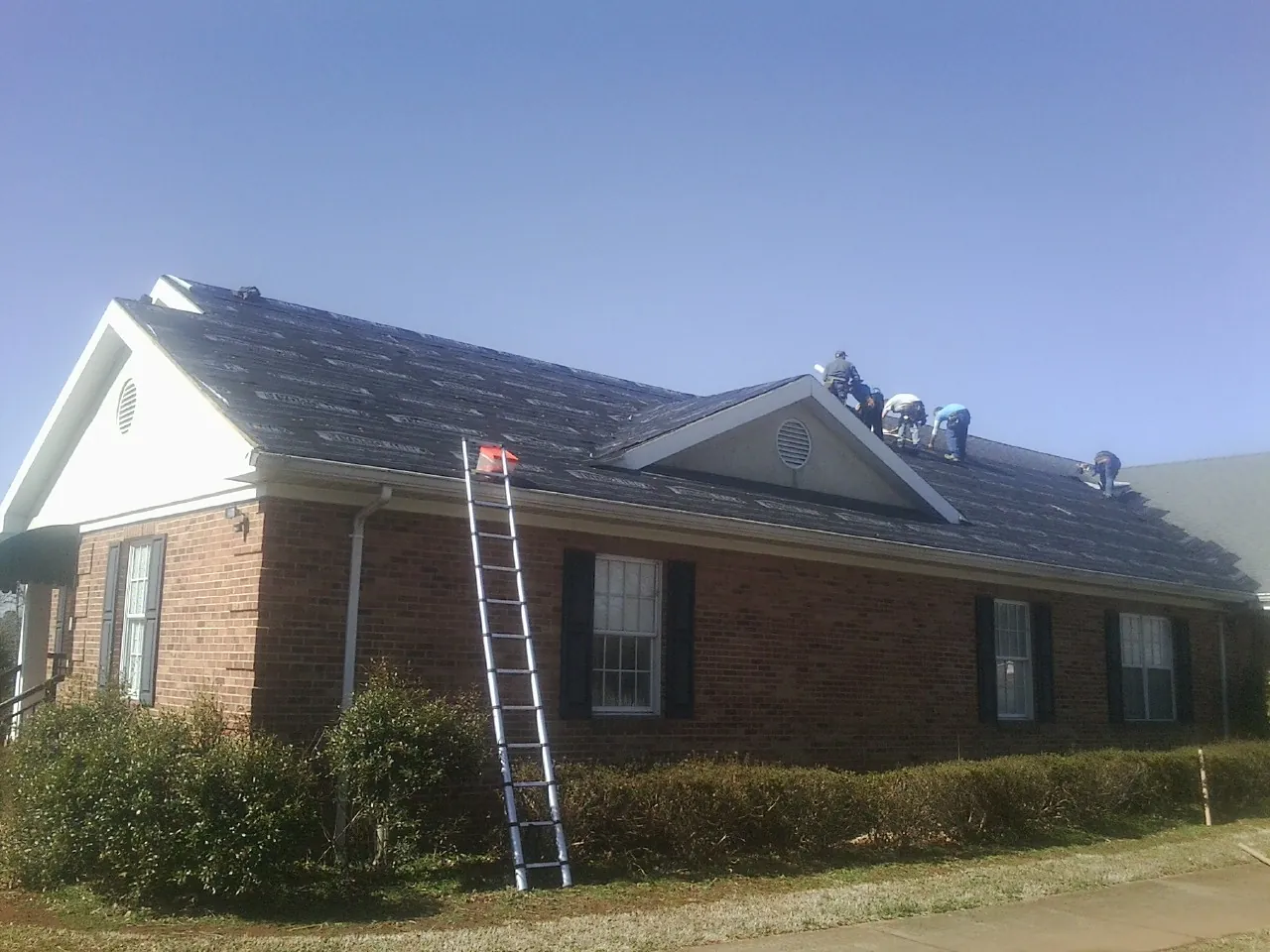 Crew tearing shingles off a brick ranch roof with a ladder set — Emergency Roof Repair work by our crew in Sunnyside