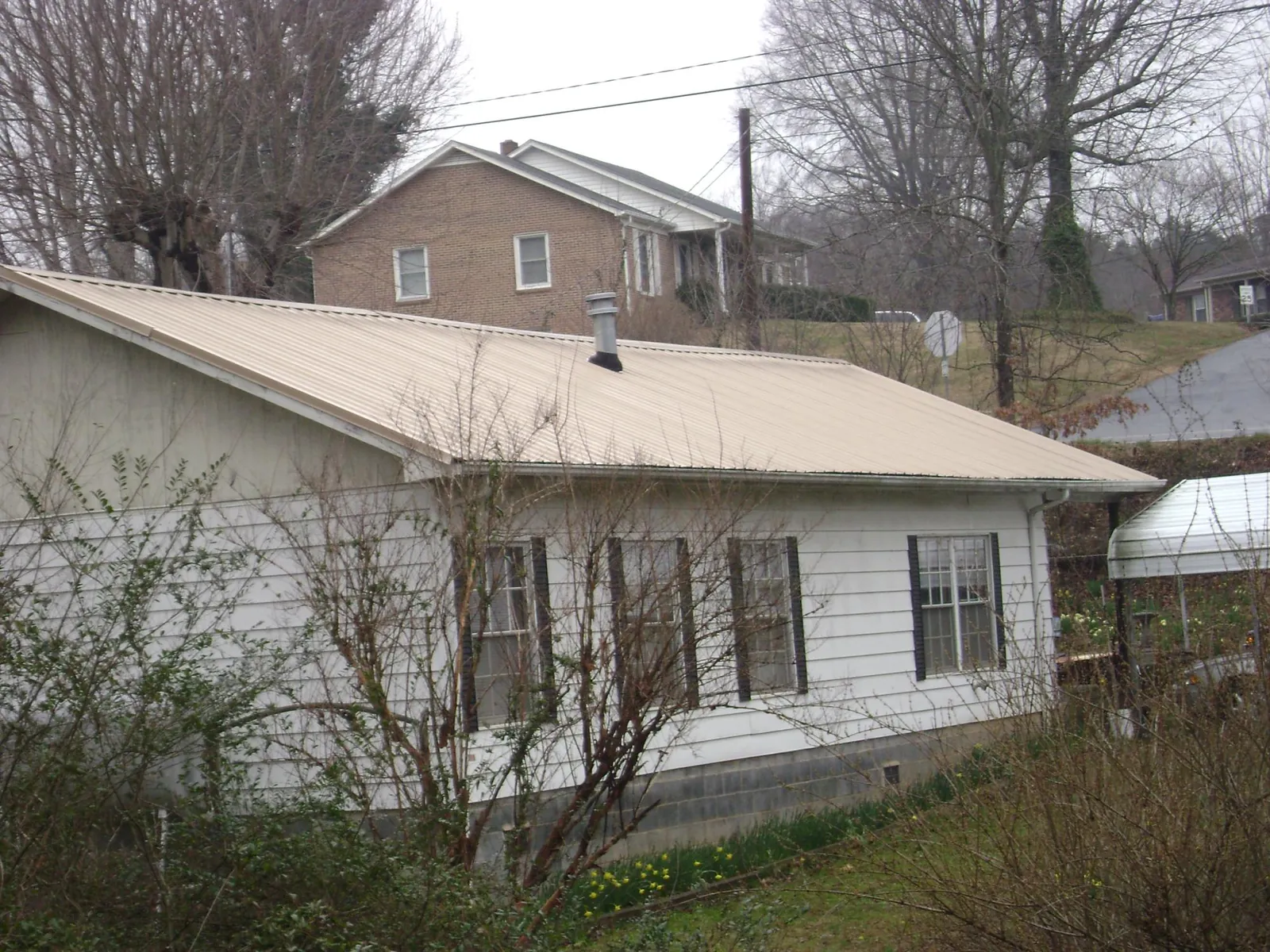 Tan metal roof on a white sided house set into a hillside — Commercial Roofing by Roofing Brothers in Sunnyside