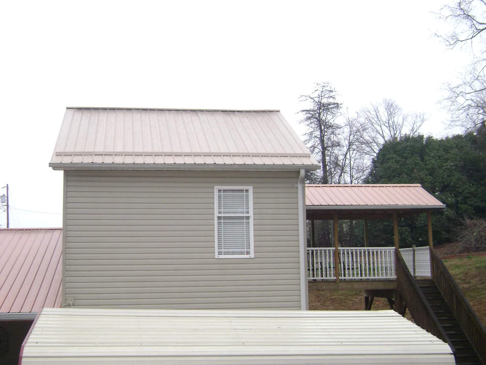 Tan metal roofs on a two story addition and attached porch, from a Roof Replacement job in Sunnyside